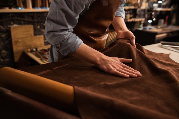 Close up of a male shoemaker working with leather textile at his workshop
